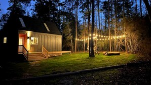 En stuga med en veranda, ett picknickbord och ljusslingor, belägen i ett skogsområde.