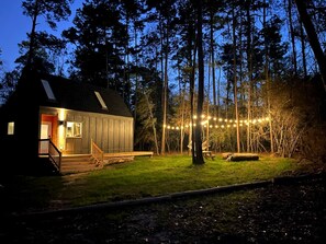 A cabin with a porch, a picnic table, and string lights in a forested area. - Gorgeous Cozy Cabin in Montgomery, Texas (Montgomery)