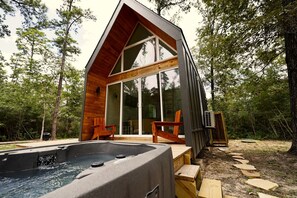 Eine moderne Holzhütte mit Whirlpool, Holzterrasse und großen Glasfenstern.