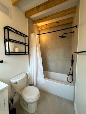 A bathroom with a toilet, a bathtub, a shower, and a shelf with toiletries. - Gorgeous Cozy Cabin in Montgomery, Texas (Montgomery)