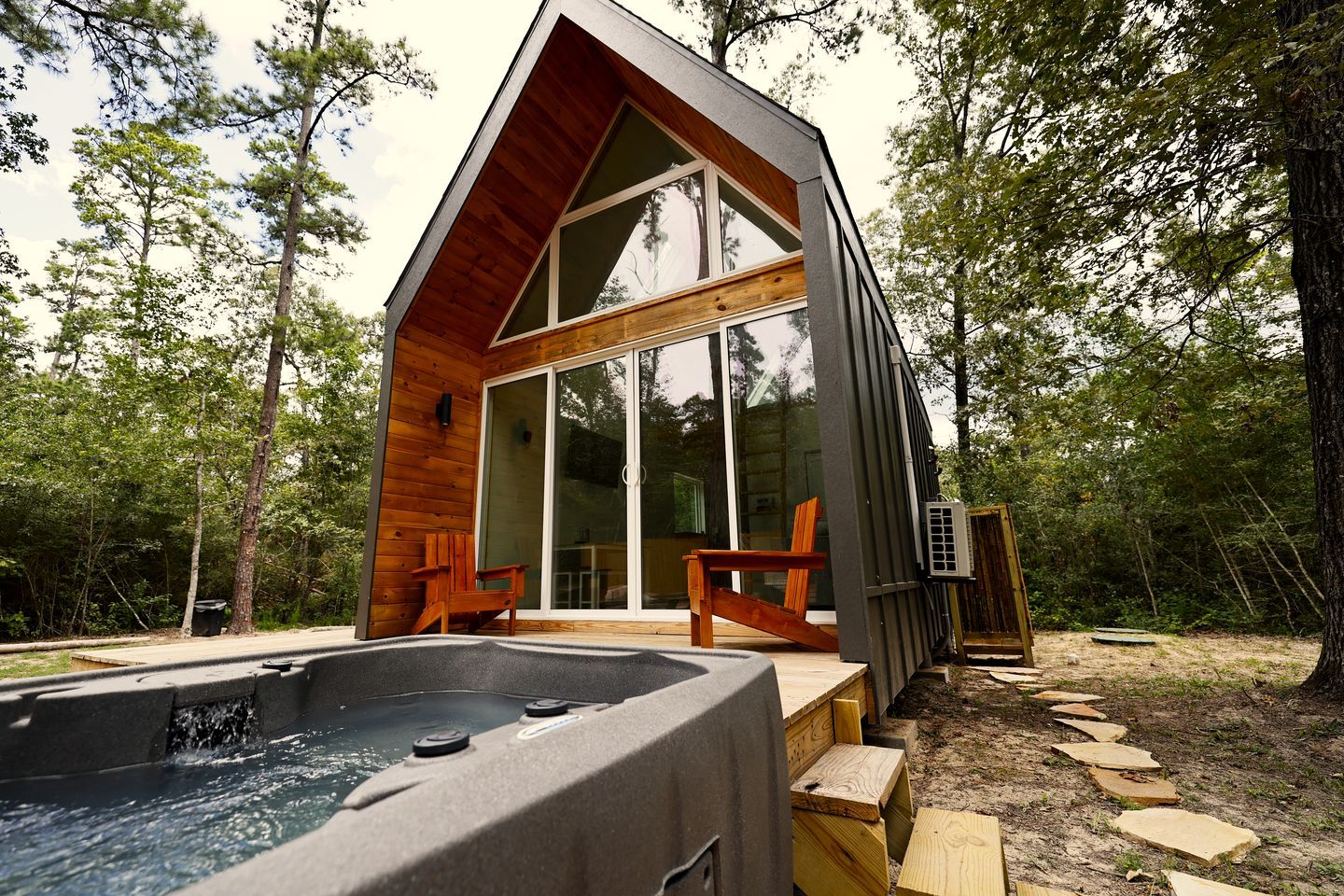 A modern cabin with a hot tub, wooden deck, and large glass doors.