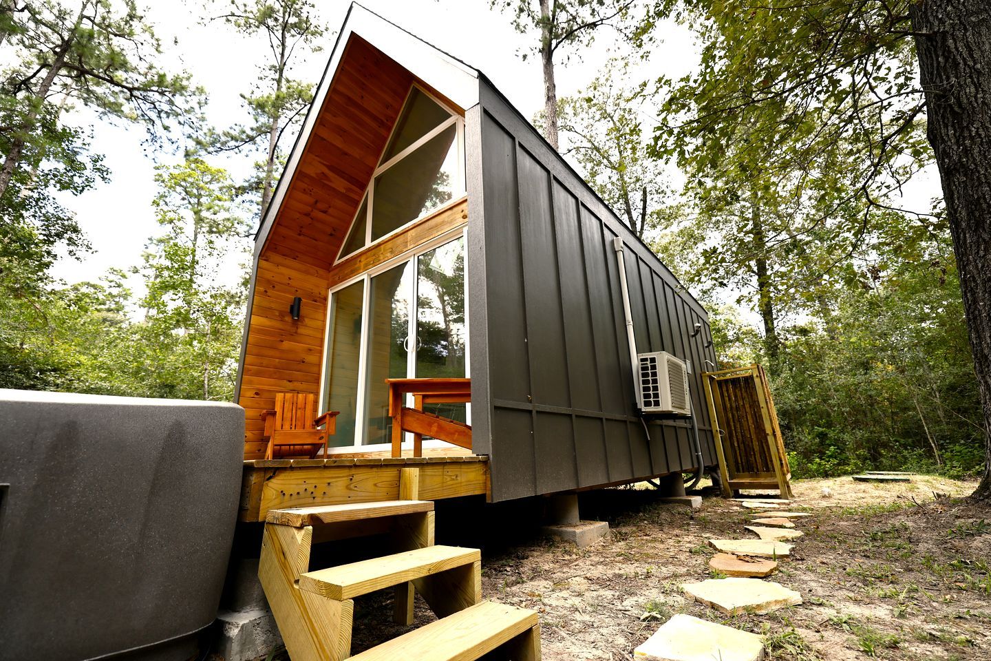 A cabin with a wooden deck, a large sliding glass door, and a small outdoor seating area.
