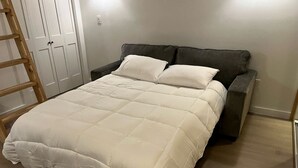 Uma cama com edredom branco, cabeceira escura e escada de madeira.