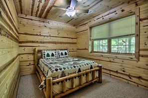 Ein Zimmer in einer Holzhütte mit einem Bett, einem Fenster und einem Deckenventilator.