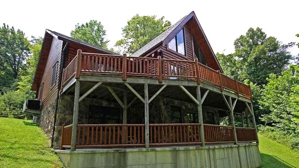 Eine Holzhütte mit Balkon, Steinfundament und umgeben von Grün.