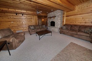 Ein rustikales Blockhaus-Interieur mit Kamin aus Naturstein, Ledersofas und Deckenventilator.