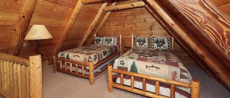 Une chambre mansardée chaleureuse avec deux lits en bois, une rambarde en bois et une lampe.