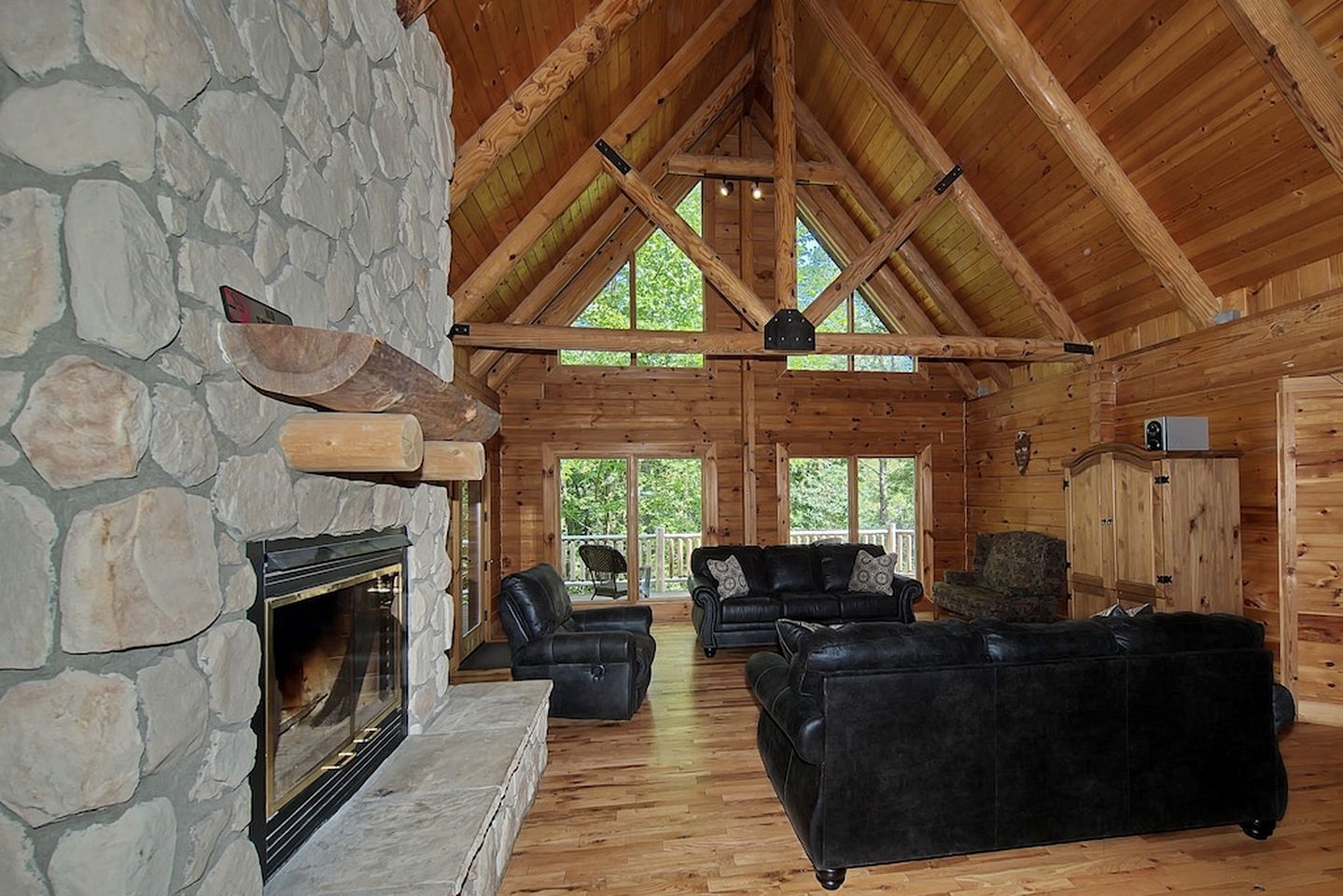 A log cabin interior with a stone fireplace, wooden ceiling beams, and a stone wall.