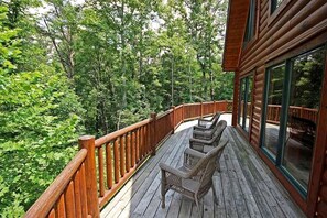 A wooden deck with wicker chairs, surrounded by a forested area. - Rural Cabin with Spa Nestled into the Woods in Ohio (Rockbridge)
