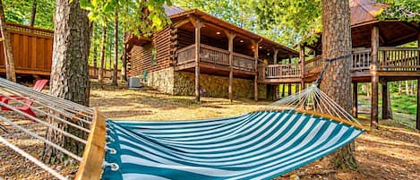 A wooden cabin with a hammock, surrounded by trees and a stone wall.