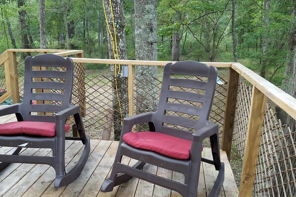 Two rocking chairs on a wooden deck with a view of a forest.