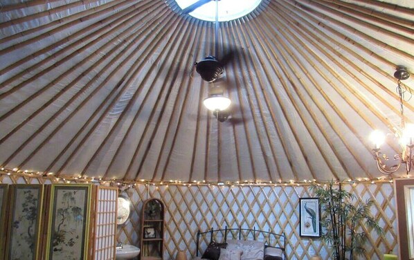 A yurt interior with a central light fixture, a bed, and decorative elements.