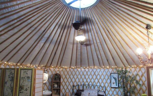 A traditional yurt interior with a central light fixture, a bed, and decorative elements.