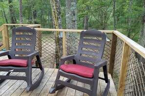 Two rocking chairs on a wooden deck with a view of a forest. - Rustic Luxury: Riverfront Yurt Glamping in Claxton, Georgia (Claxton)
