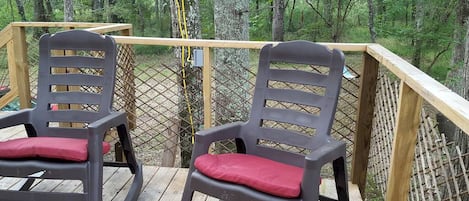 Two rocking chairs on a wooden deck with a view of a forest.