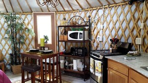 A compact kitchen with a stove, microwave, and a small dining area with chairs. - Rustic Luxury: Riverfront Yurt Glamping in Claxton, Georgia (Claxton)