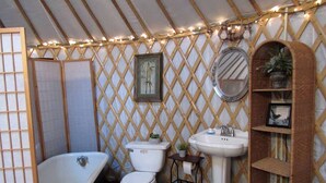 A bathroom with a bathtub, toilet, sink, and a lattice wall with string lights. - Rustic Luxury: Riverfront Yurt Glamping in Claxton, Georgia (Claxton)