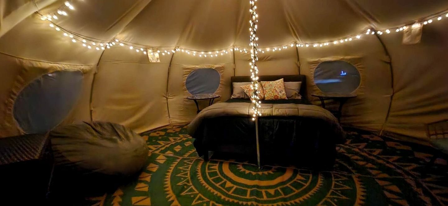 Una carpa con una cama, almohadas, una mesita y luces colgantes.