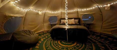 Una carpa con una cama, almohadas, una mesita y luces colgantes.