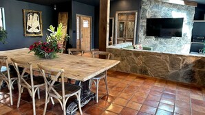 A dining area with a wooden table and chairs, a stone wall with a TV, and a tiled floor. - Stunning Yurt for a Romantic Getaway in Dripping Springs, Texas (Dripping Springs)