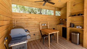 A wooden cabin with a ceiling fan, a grill, a table, chairs, a sink, and a small kitchen area. - Stunning Yurt for a Romantic Getaway in Dripping Springs, Texas (Dripping Springs)