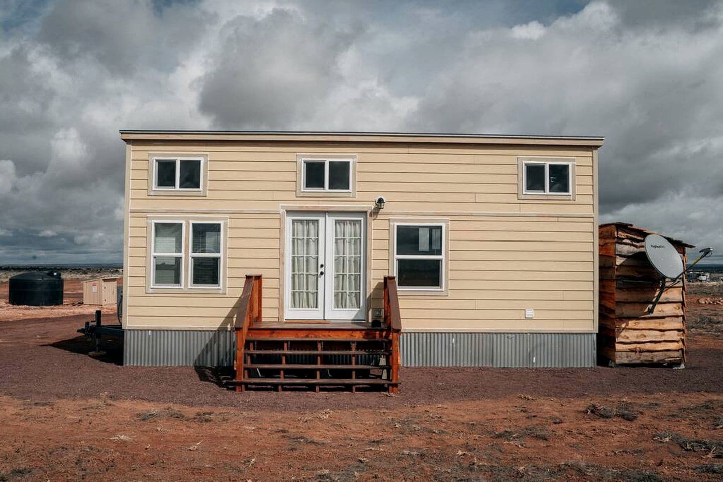 Une maison à deux étages avec un porche à l’avant, une antenne parabolique et un réservoir d’eau en arrière-plan.