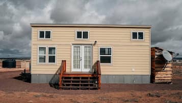 Une maison à deux étages avec un porche à l’avant, une antenne parabolique et un réservoir d’eau en arrière-plan.