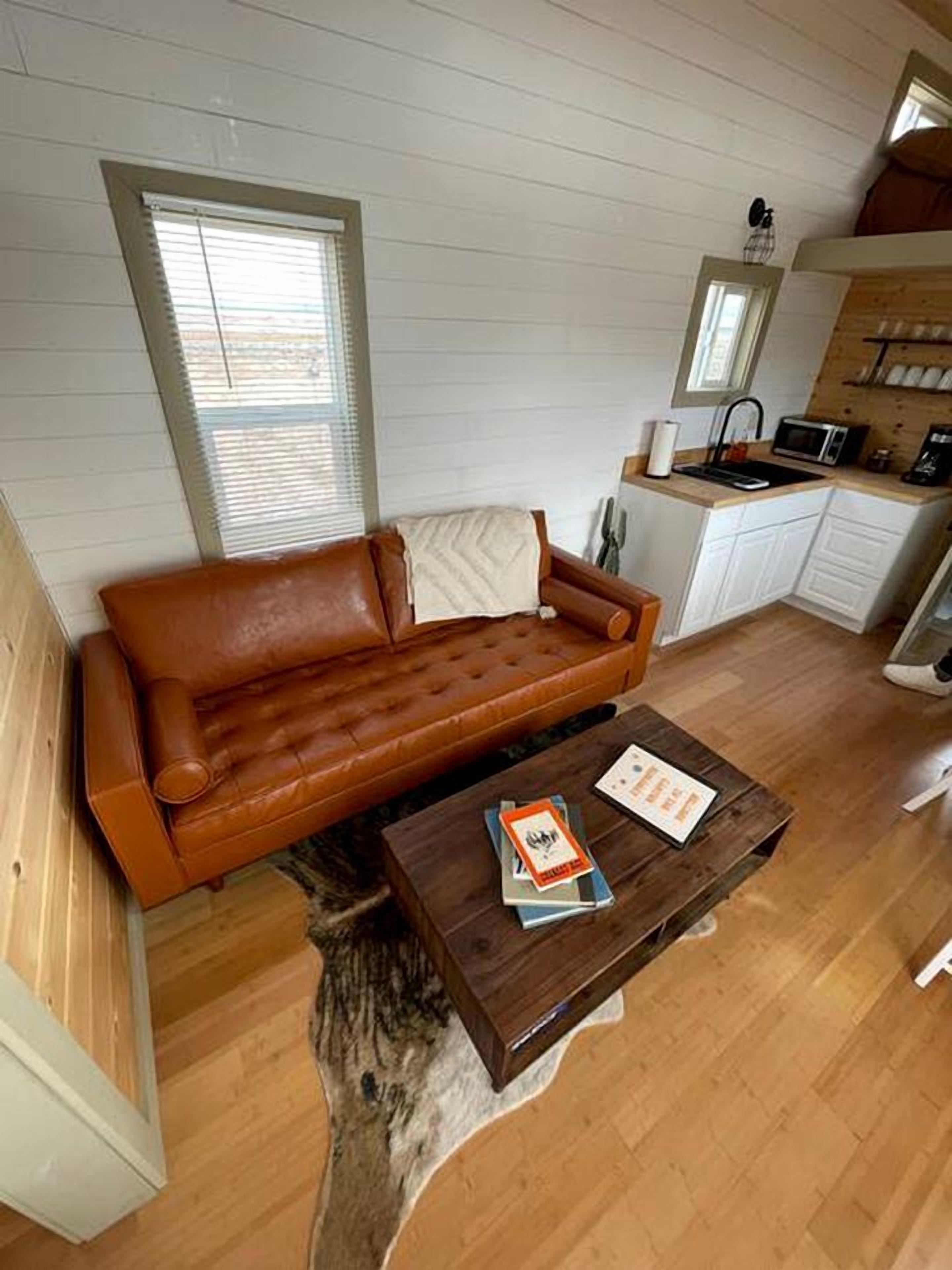 A cozy room with a brown leather sofa, a wooden coffee table, and a kitchen area with white cabinets and a microwave.