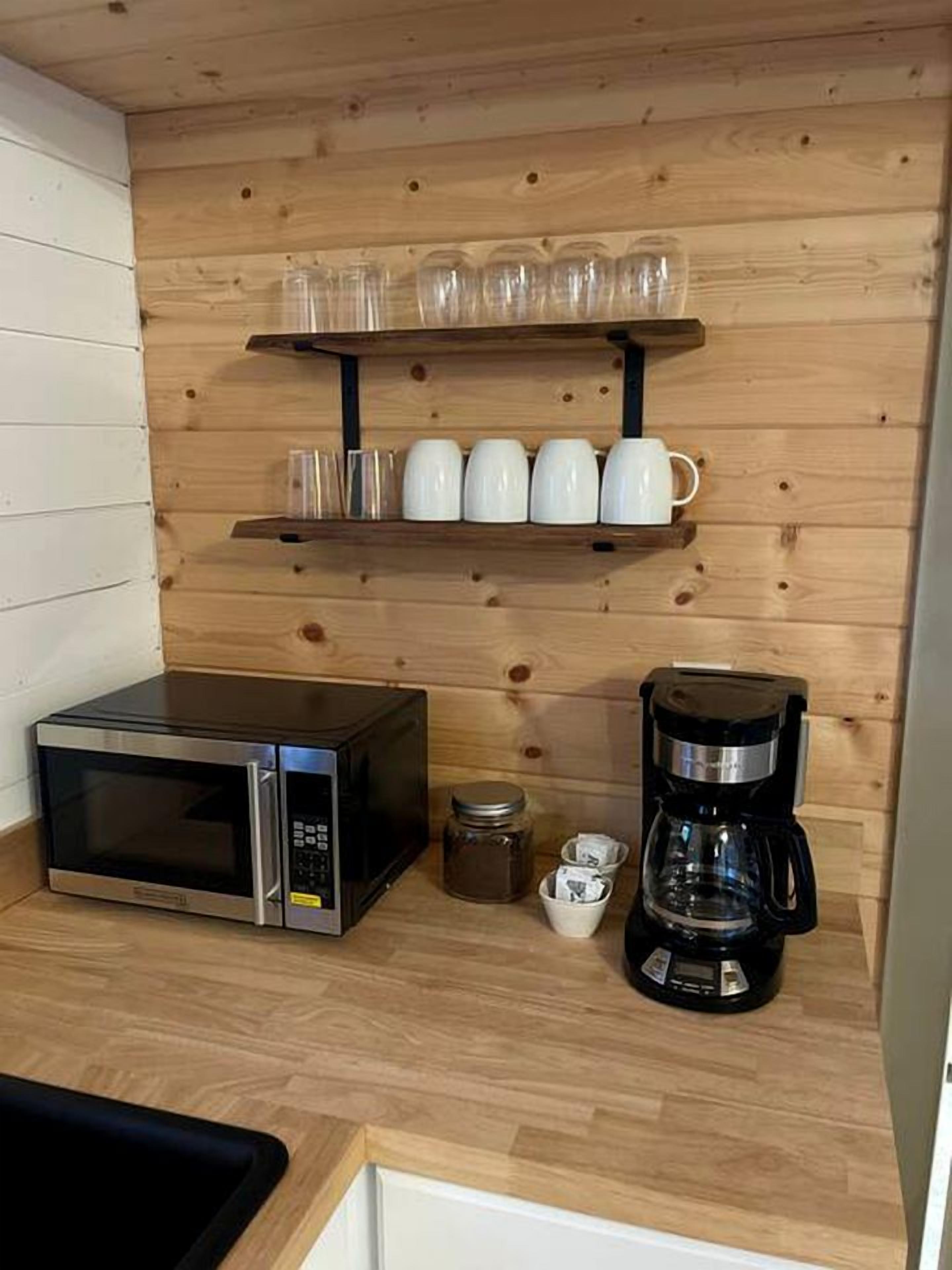A kitchenette with a microwave, coffee maker, and a shelf with cups and glasses.