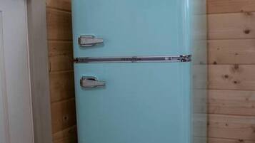 A light blue refrigerator in a room with wooden walls and a wooden floor.