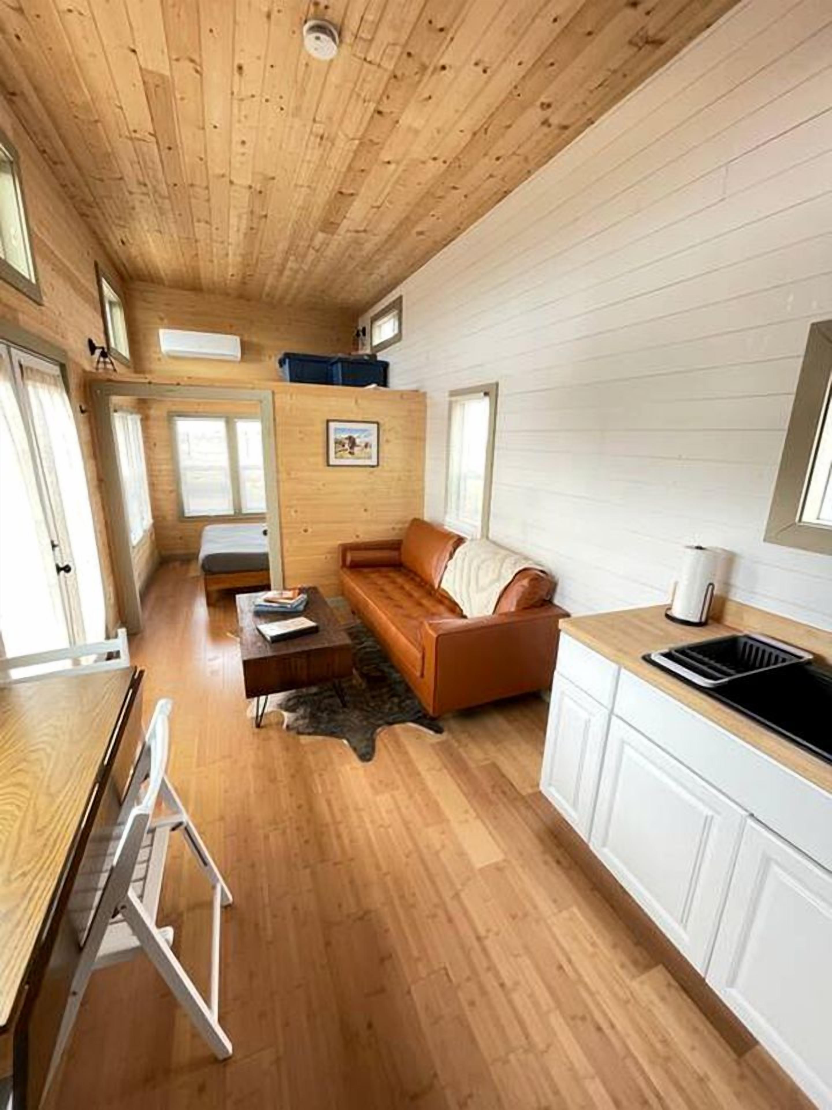 A compact cabin-style room with a wooden ceiling, a sofa, a dining table, and a kitchenette.