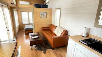 A compact cabin-style room with a wooden ceiling, a sofa, a dining table, and a kitchenette.