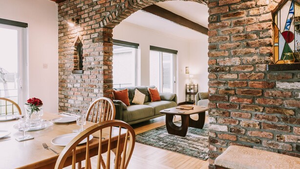 A dining area with a brick archway, wooden furniture, and a green sofa in the background. - Spacious Strandhill House with Knocknarea Views (Strandhill)