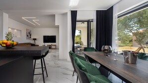 A modern living room with a dining area, a TV, and a fruit bowl on the counter. - Villa Karla with pool&sea view by Villas Guide (Banjol)