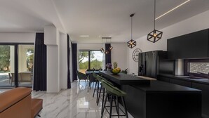 A modern kitchen with a central island, bar stools, pendant lighting, and a large window offering a view of the outdoors. - Villa Karla with pool&sea view by Villas Guide (Banjol)