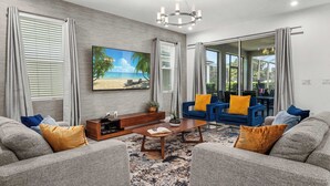 Uma sala de estar moderna com uma grande televisão de tela plana, um sofá azul, uma mesa de centro de madeira e um tapete cinza estampado.