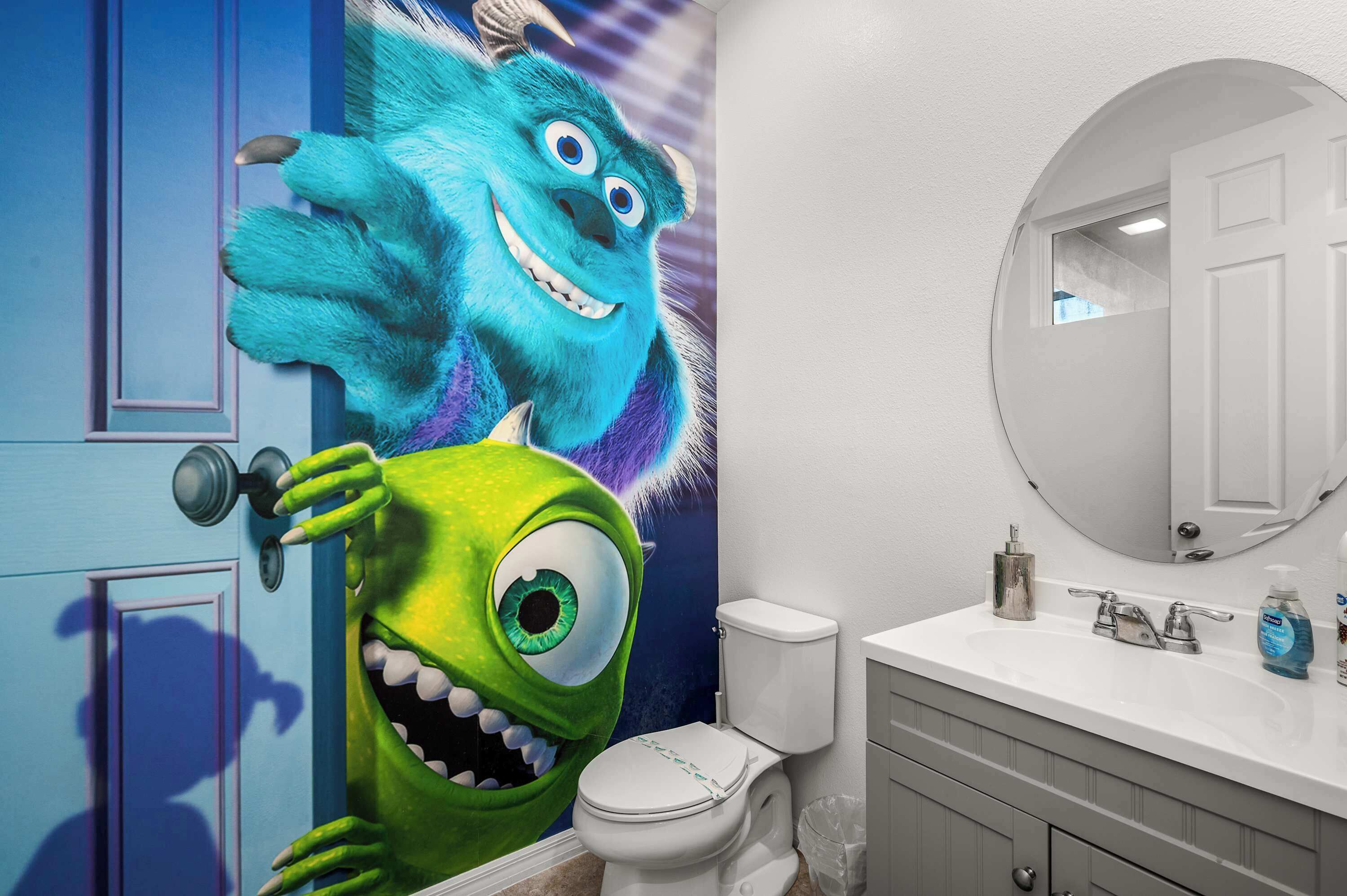 Ein Badezimmer mit einem großen Wandgemälde im Cartoon-Stil, einer weißen Toilette, einem Waschbecken mit Spiegel und Toilettenartikeln auf der Ablagefläche.