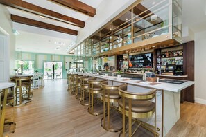 Un'area bar moderna con sgabelli alti, un bancone e un grande schermo che mostra contenuti sportivi.