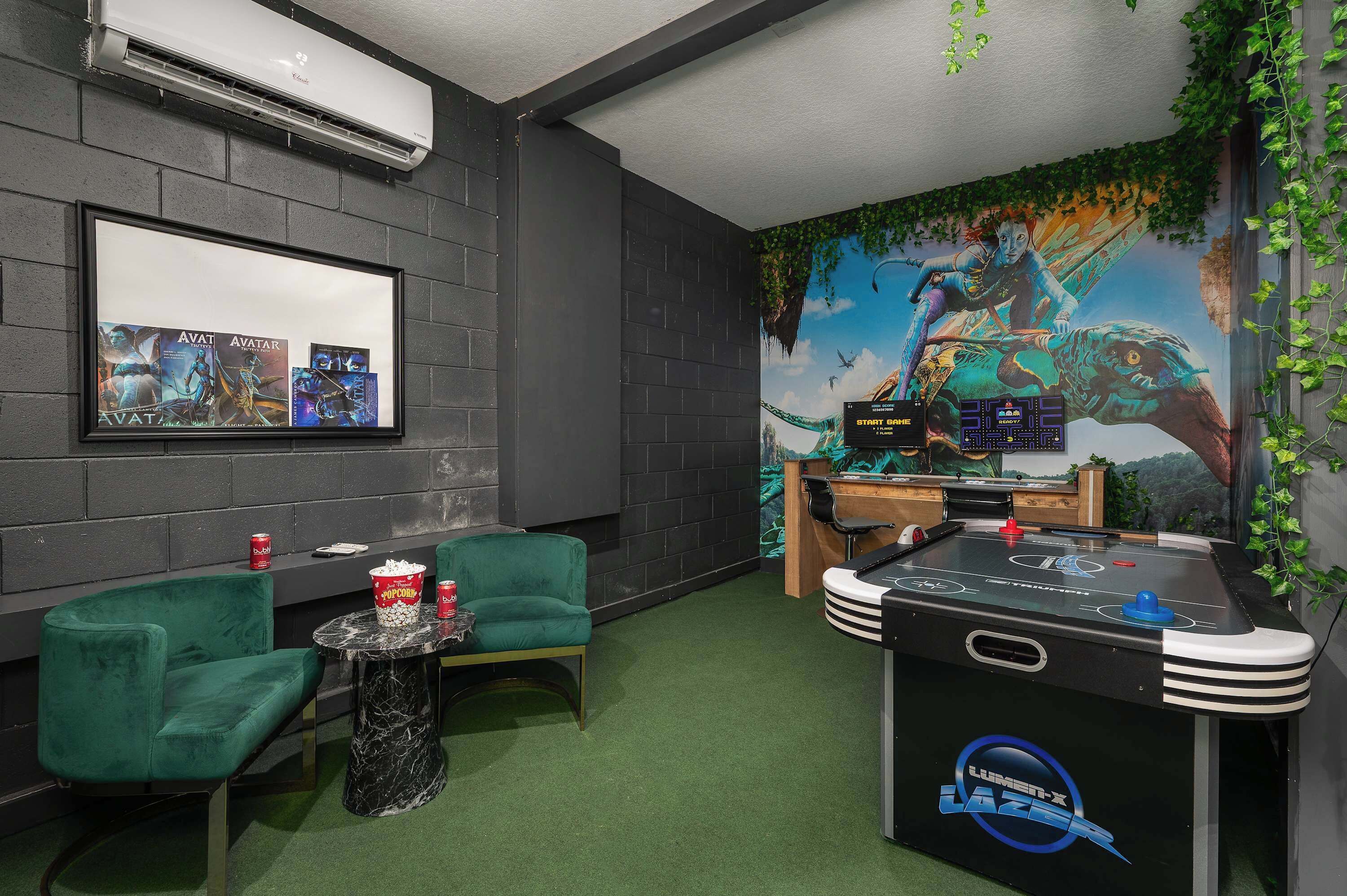 A room with a foosball table, green chairs, a projector screen, and a mural.