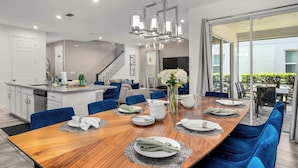 Uma sala de jantar moderna com uma mesa de madeira posta para seis pessoas, cadeiras azuis e um candelabro.