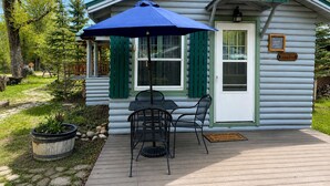 A log cabin with a patio, a table with chairs, and a blue umbrella.