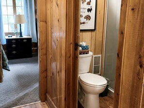 A wooden-paneled bathroom with a toilet, a framed animal illustration, and a window with curtains.