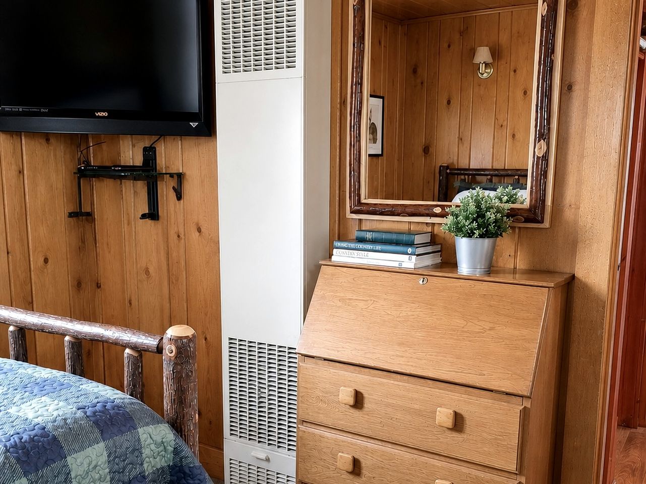 A wooden room with a bed, a dresser, a television, and a mirror.