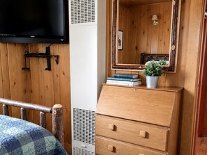 A wooden room with a bed, a dresser, a television, and a mirror.