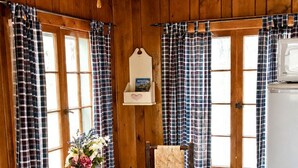A wooden interior with a dining table, chairs, a stove, and plaid curtains.