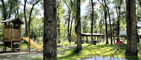 Un parque infantil con una estructura de juego de madera y un tobogán, rodeado de árboles.