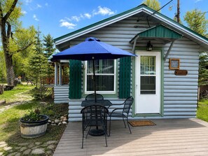 Eine Holzhütte mit einer Terrasse, einem Tisch und Stühlen sowie einem blauen Sonnenschirm.