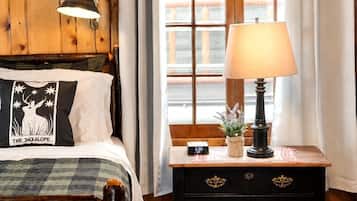 A wooden-paneled room with a bed, a nightstand, a lamp, and a window with curtains.
