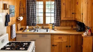 Een keuken in blokhutstijl met houten wanden, een fornuis, een plafondventilator en een raam met gordijnen.