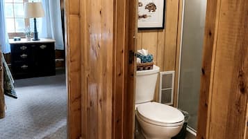 Een betegelde badkamer met toilet, een lijst met een dierillustratie, en een raam met gordijnen.